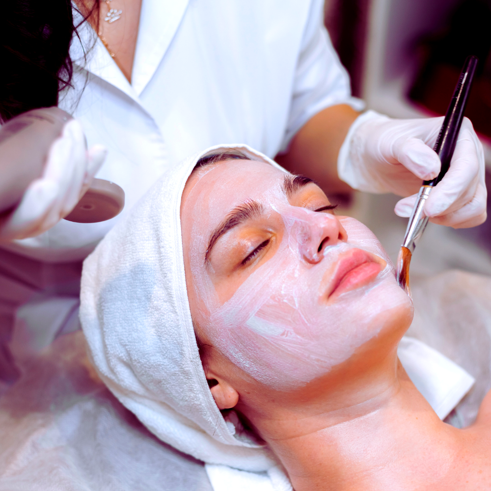 Professional applying a vegan facial mask on relaxed client.