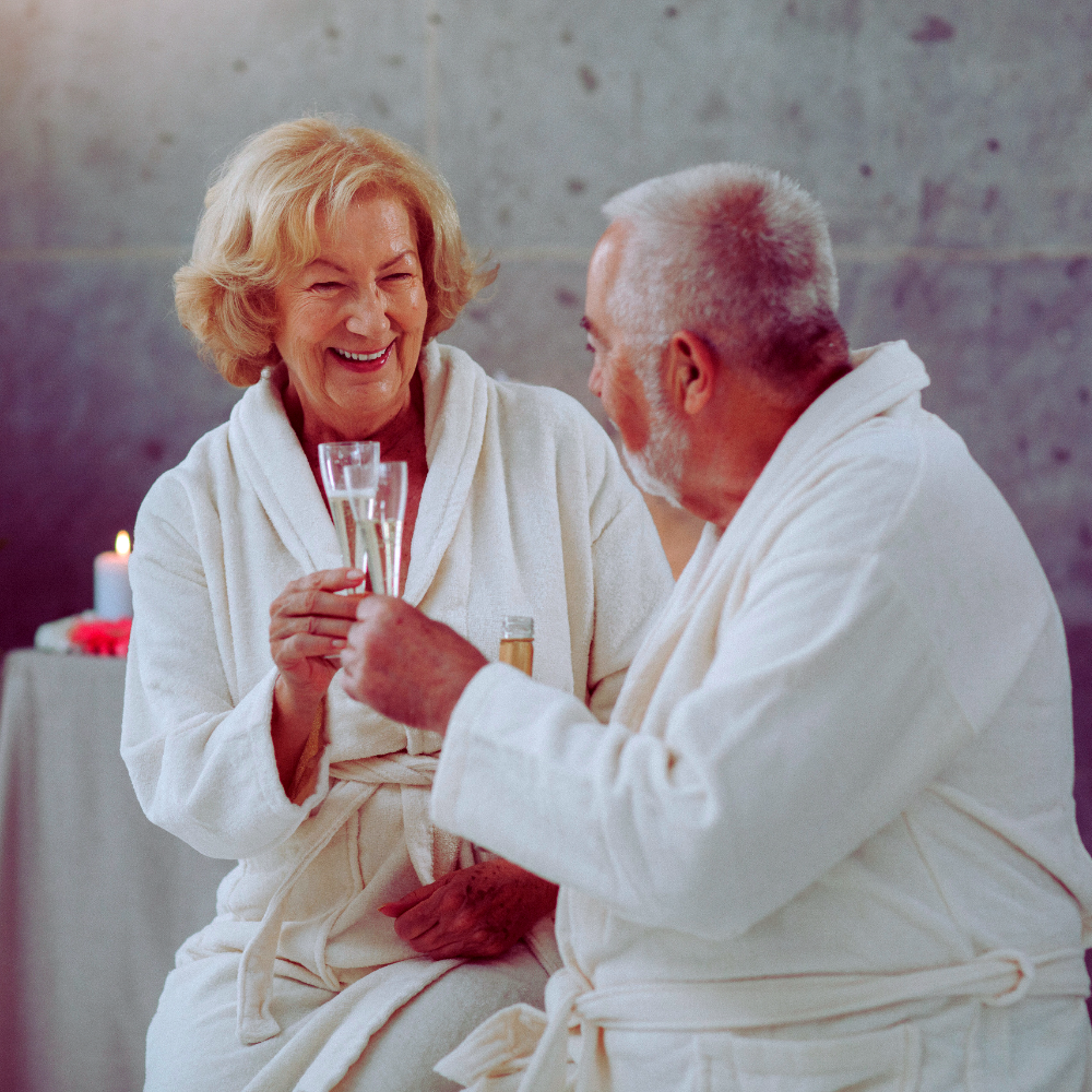 Senior couple toasting with champagne in spa robes.