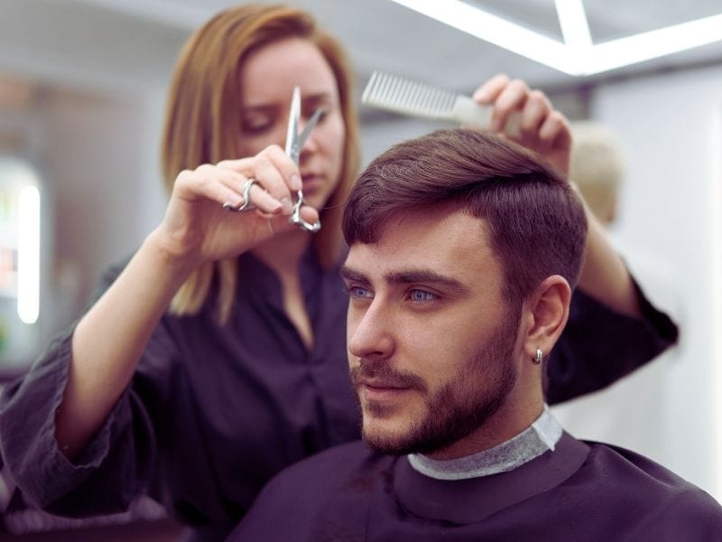 A stylist trims a man’s hair in a salon, highlighting precision and the use of quality hair beauty products.