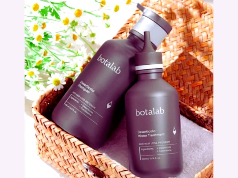 Two Botalab bottles in a woven basket surrounded by flowers, promoting organic hair treatments.