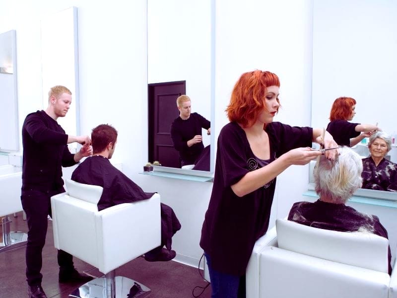 Hair stylists working with clients in a modern salon, showcasing haircare innovation to retain clients with personalized services.