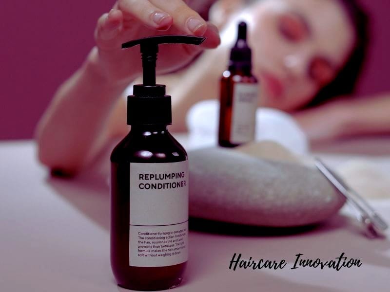 A bottle of replumping conditioner paired with essential oils and natural stones, symbolizing haircare innovation.