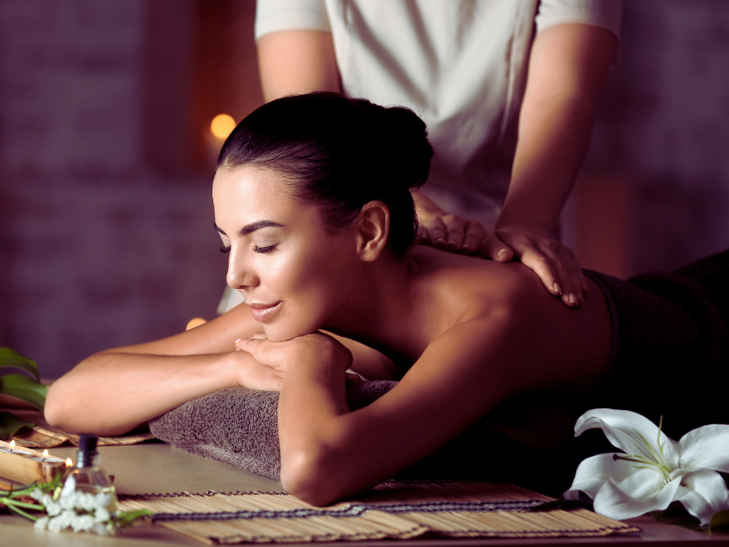 A woman enjoying a relaxing back massage in a tranquil spa setting, surrounded by flowers and soft lighting.