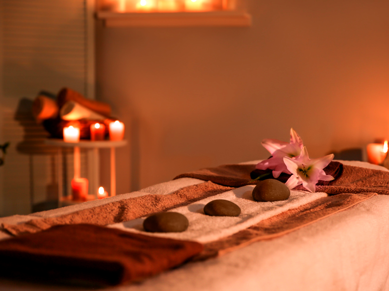 A serene spa scene with a massage table, stones, lilies, and candlelight. 