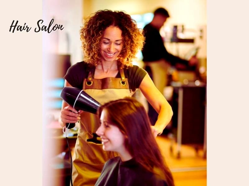 A smiling hairstylist blow-drying a client's hair in a modern hair salon, promoting sustainable haircare practices.