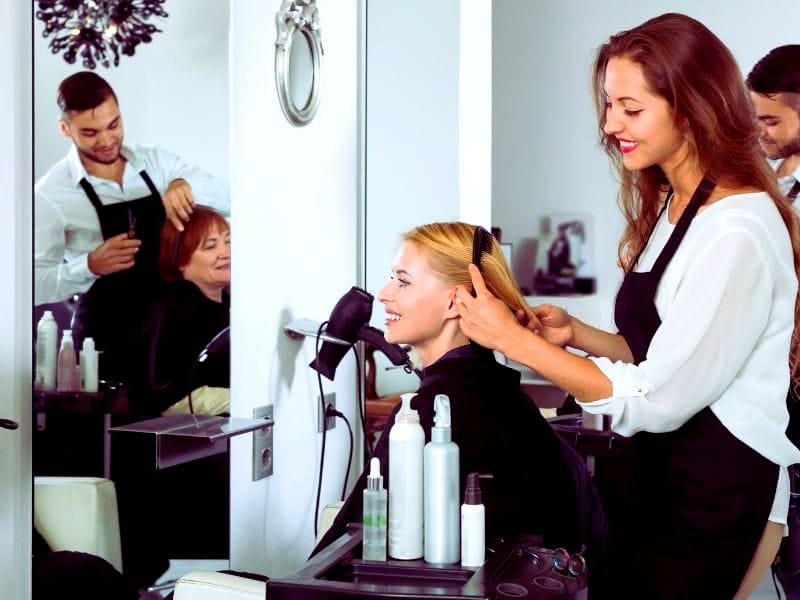 Hairstylists working with clients; hair products on counter raise concerns about toxic hair products.