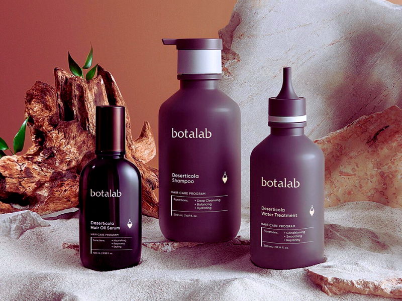 Botanical-inspired Botalab vegan haircare products, including shampoo, treatment, and oil serum, displayed elegantly against a natural wood and stone background.