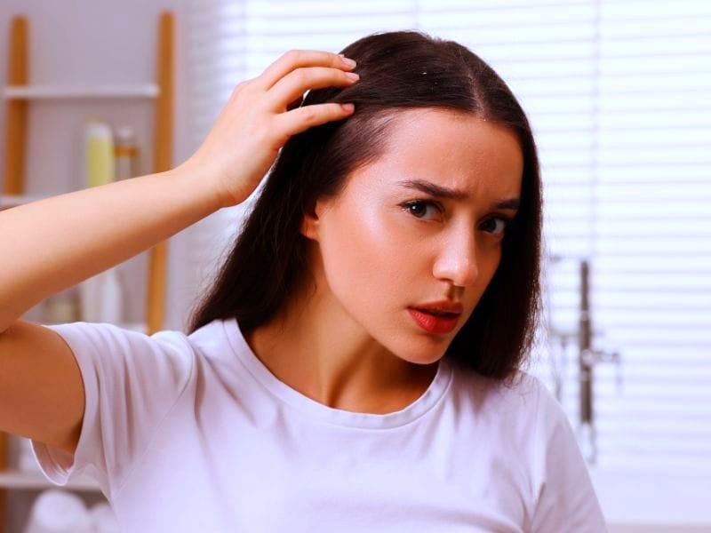 Concerned woman inspecting her scalp, emphasizing the benefits of 'plant-based hair care' for healthier hair.