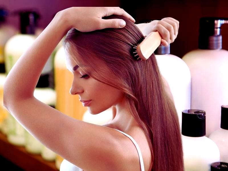 Woman brushing her healthy hair surrounded by salon bottles, promoting ways to boost salon revenue and client satifaction.