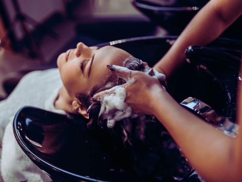 Client enjoying a relaxing shampoo treatment with clean beauty haircare products in a modern salon setting.