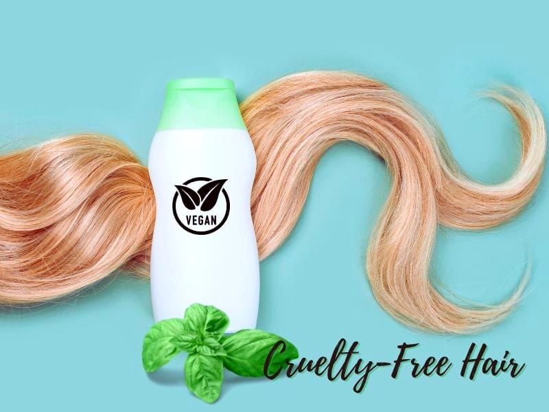 A white bottle of vegan shampoo with a green cap, next to a strand of blonde hair and a sprig of basil, on a light blue background. Cruelty-free hair products.