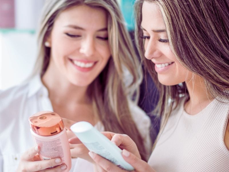 Two smiling women examining cruelty-free shampoo bottles, highlighting a commitment to ethical beauty choices.