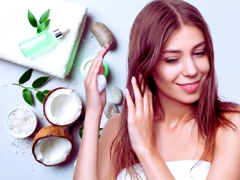 A smiling woman applying natural hair care products, surrounded by organic ingredients like coconut, leaves, and essential oils.