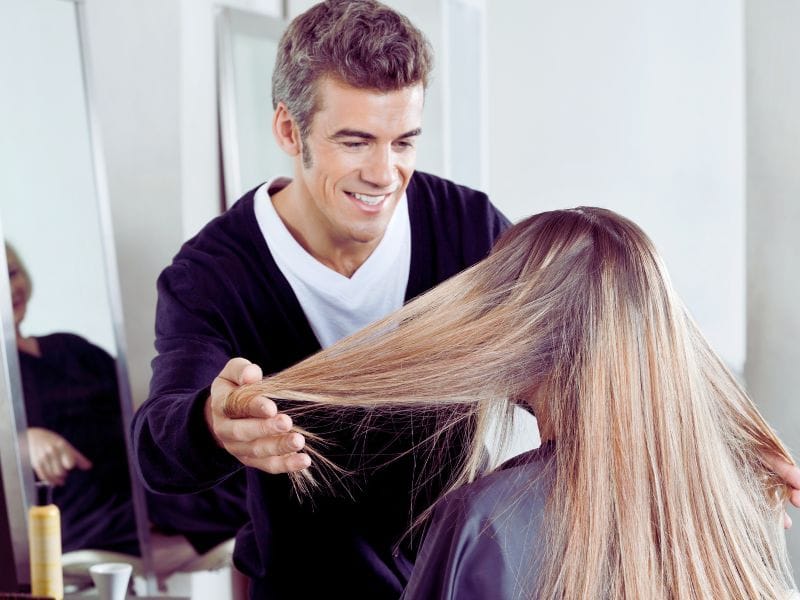 A hairstylist examining a client's sleek, smooth hair in a salon, highlighting the results of a professional frizz-fighting treatment