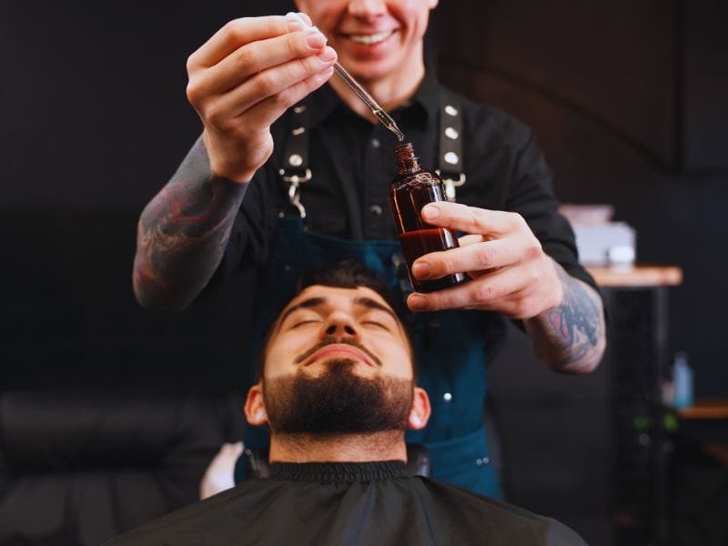 Barber applying anti-frizz oil to a relaxed client, promoting hydration and smoothness for frizz-free facial hair.