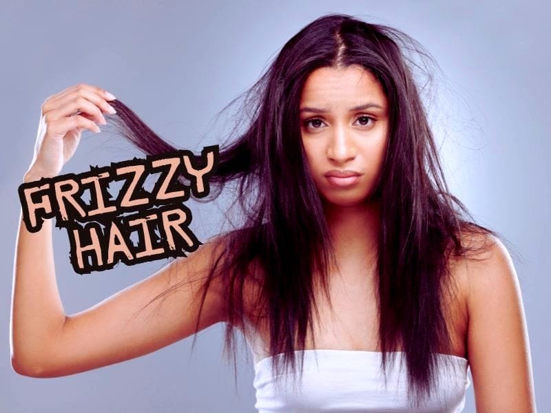 Frustrated woman with frizzy, dry hair holding a section of tangled strands, emphasizing hair care concerns and solutions.