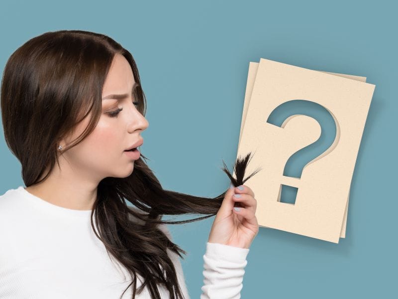 Concerned woman hair with a puzzled expression, questioning hair damage and dryness on a muted blue background.