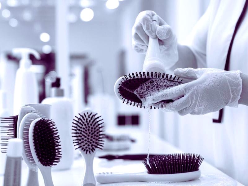 A professional cleaning hairbrushes with soap and gloves, ensuring the best hairbrushes for salons.