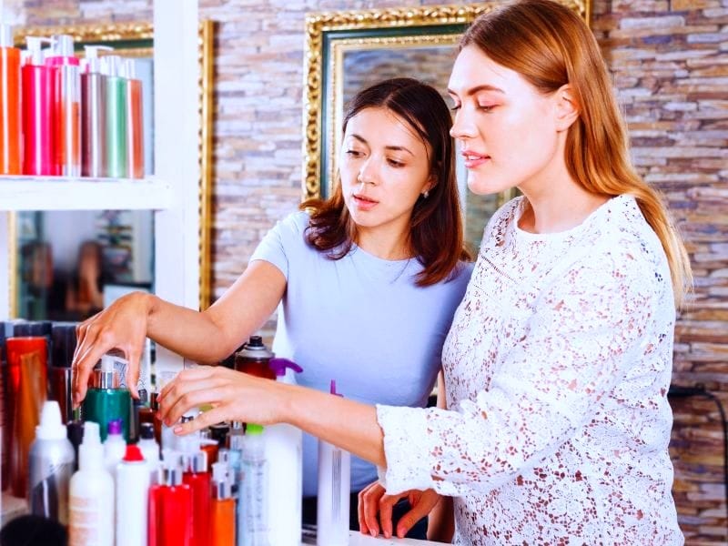 Two women browsing hair care products in a salon, discussing and selecting the best options for their hair needs