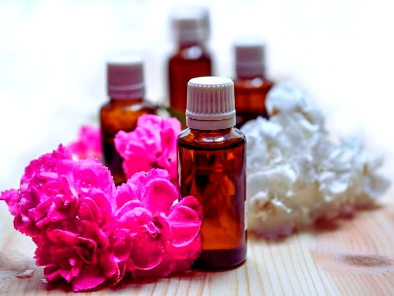 Bottles of essential hair oil surrounded by fresh pink and white flowers, promoting natural hair care benefits.