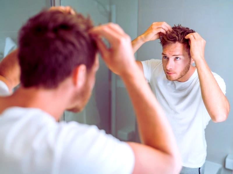 A young man examining his hair in the mirror, focusing on hair care and grooming for healthy and stylish hair maintenance.