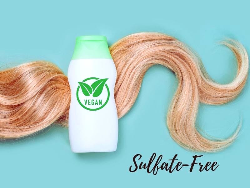 Vegan sulfate-free shampoo bottle on a green background, surrounded by smooth blonde hair strands.