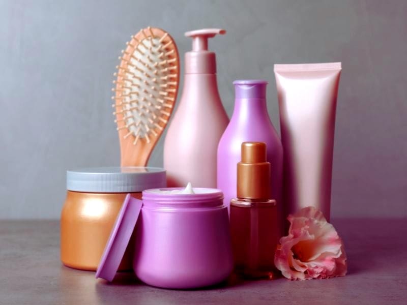 Assorted hair care products in pastel and gold tones, including jars, bottles, and a wooden brush with soft lighting.